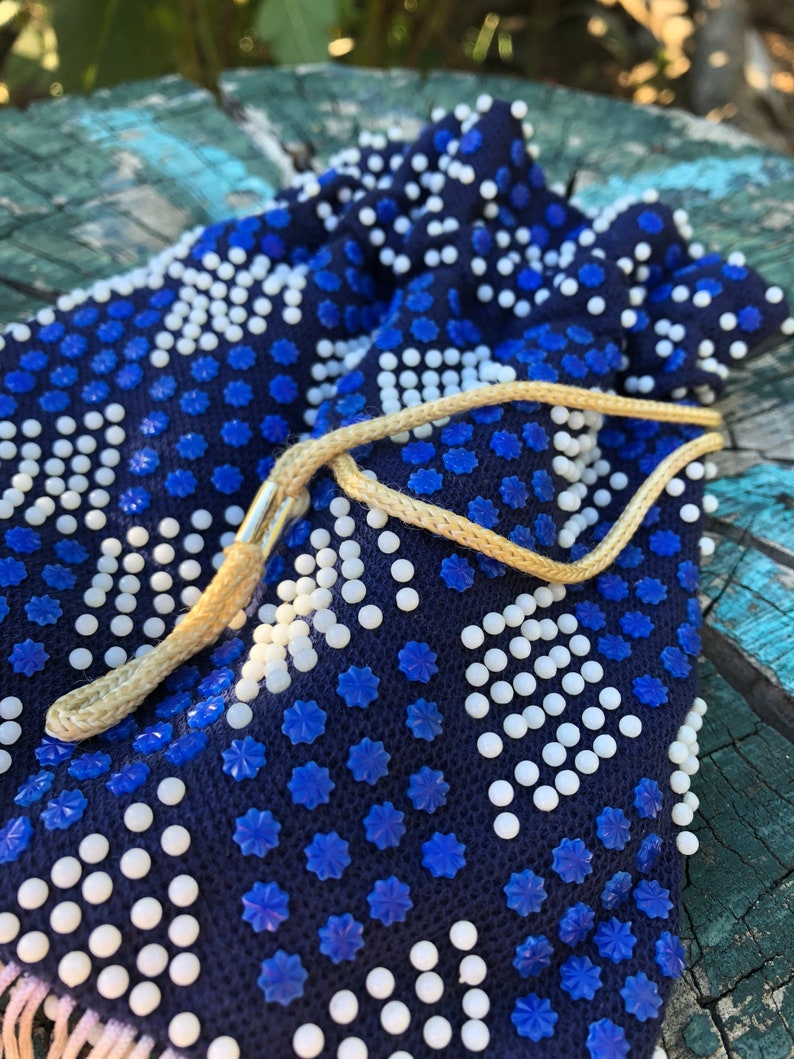 May include: A small blue drawstring bag with white and blue beads. The bag has a tan drawstring.