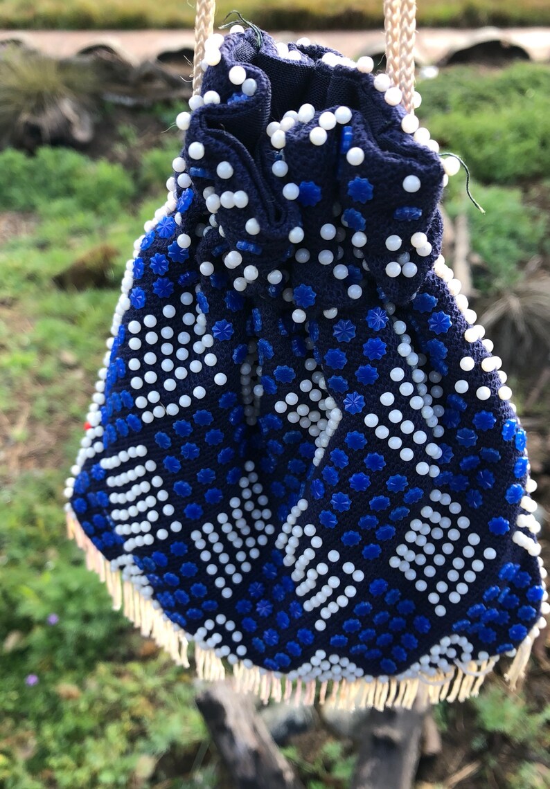 May include: A blue and white beaded drawstring bag with a fringe trim. The bag is decorated with a geometric pattern of white and blue beads.