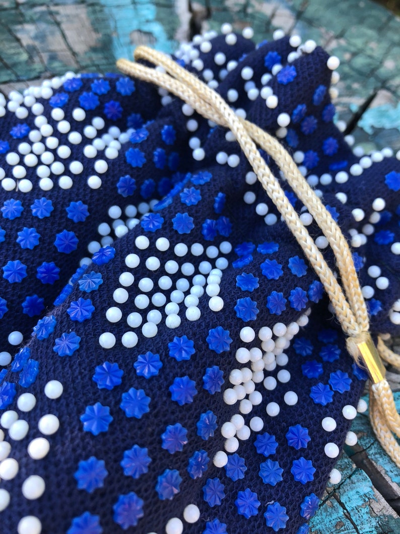 May include: A blue drawstring bag with white and blue beads. The bag is made of fabric and has a drawstring closure.