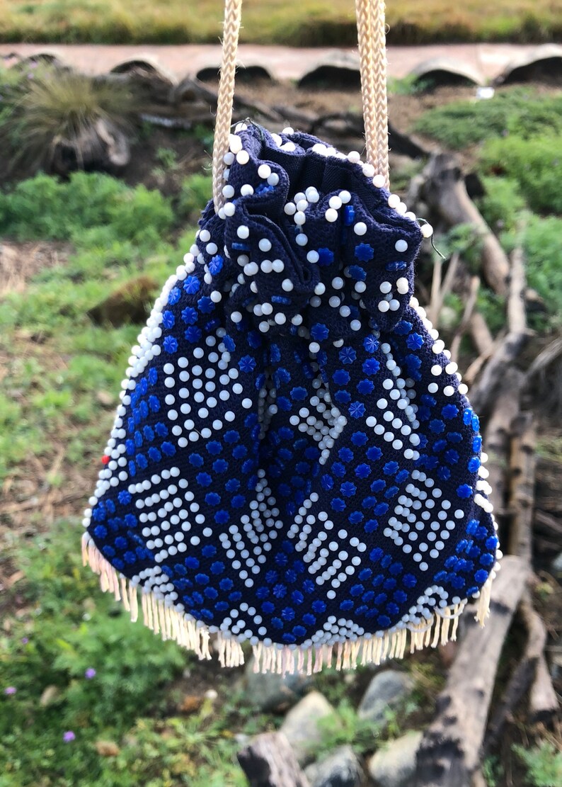 May include: A blue and white beaded drawstring bag with a fringe trim. The bag is made of small, round beads and has a geometric pattern.
