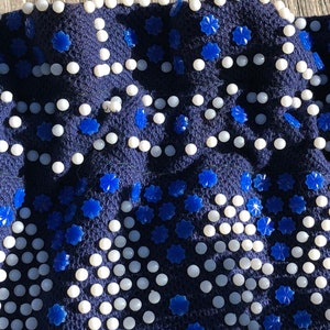 May include: A navy blue fabric with a repeating pattern of white beads and blue star-shaped embellishments.