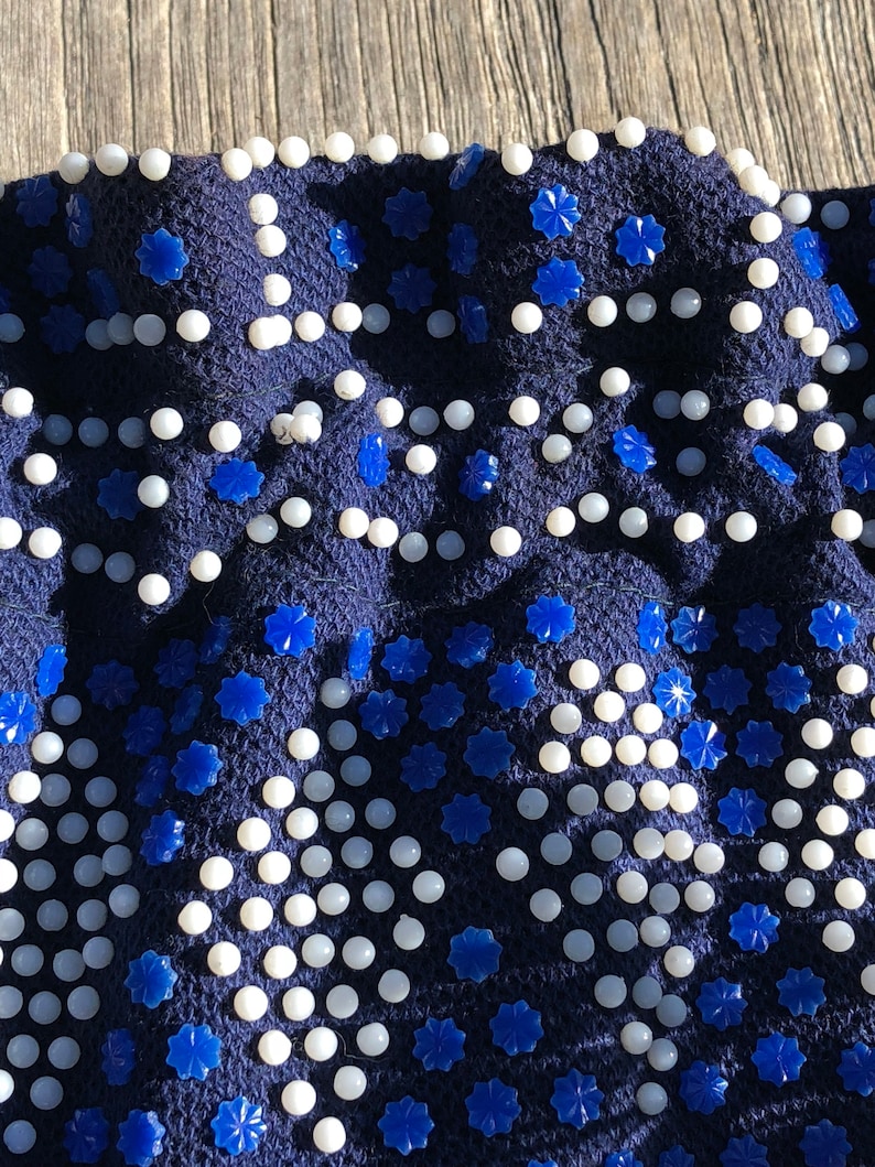 May include: A navy blue fabric with a repeating pattern of white beads and blue star-shaped embellishments.