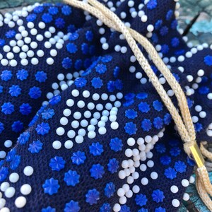 May include: A blue drawstring bag with white and blue beads. The bag is decorated with a pattern of white beads and blue stars.