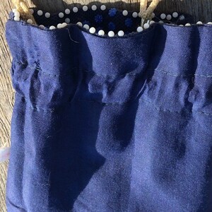 May include: A dark blue drawstring bag with a white beaded trim. The bag is made of a soft, textured fabric.