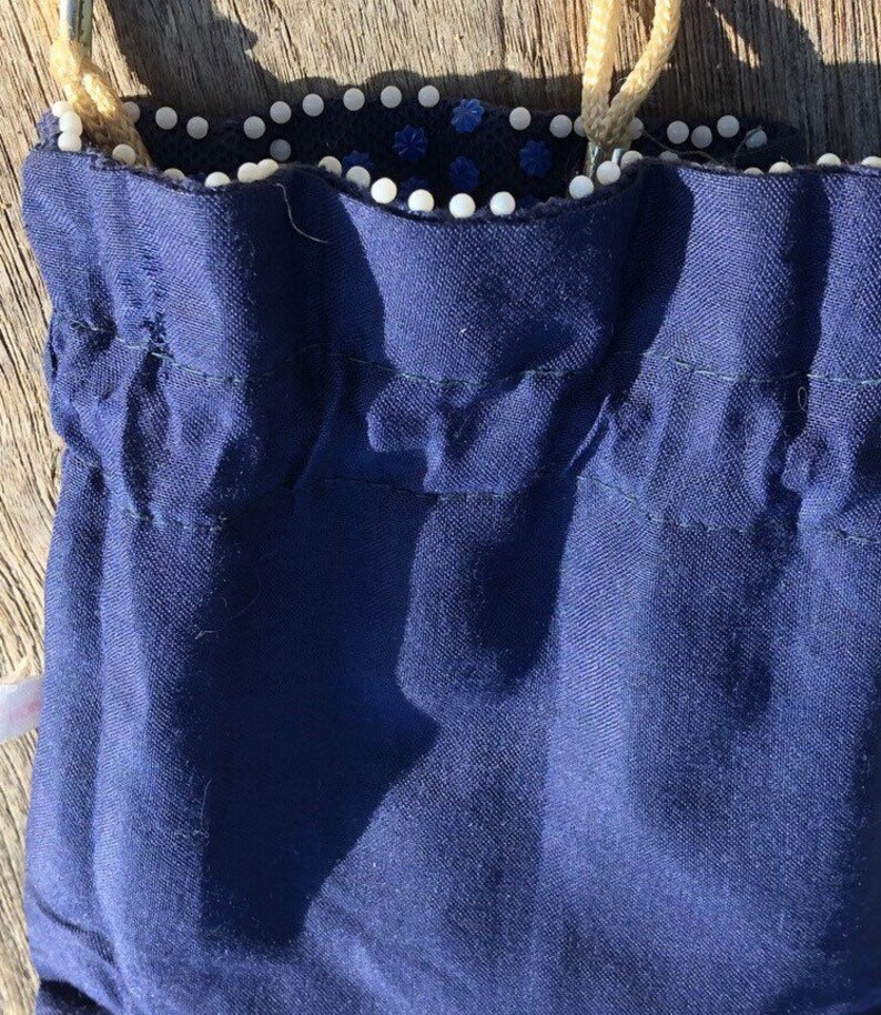 May include: A dark blue drawstring bag with a white beaded trim. The bag is made of a soft, textured fabric.