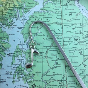 Peut inclure: Un marque-page en argent en forme de clé de sol, avec un crochet en haut. Le marque-page est posé sur une carte de la côte est du Maryland.