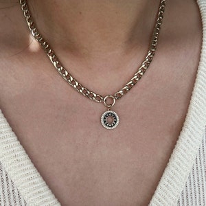 May include: Gold chain necklace with a round pendant featuring black and white stones.