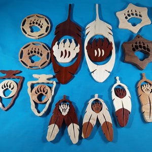 May include: A collection of 13 wooden ornaments featuring a bear paw print design. The ornaments are in various shapes, including feathers, arrowheads, and stars. The ornaments are made of different types of wood, including maple, cherry, and walnut. The ornaments are painted in natural wood tones.