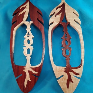 May include: Two wooden feather ornaments with the word "YOU" cut out in the center. The feathers are painted in a red and white woodgrain pattern.