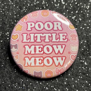 May include: Pink and yellow button with a white outline and the text "Poor Little Meow Meow" surrounded by cat and paw prints.