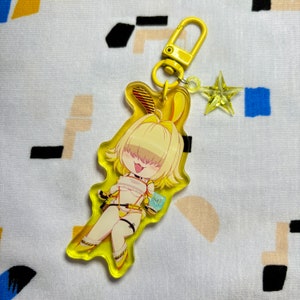May include: Yellow acrylic keychain featuring an anime character with blonde hair, wearing a yellow and black outfit, holding a drink. The character has a bunny ear headband and is posed in a sitting position. The keychain has a yellow star charm attached to the top.