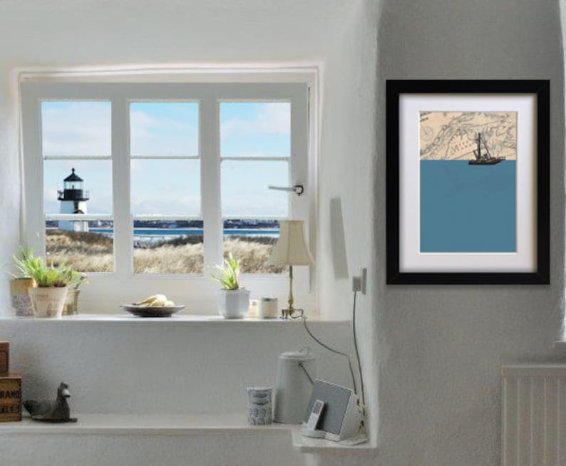 May include: A framed art print featuring a nautical theme. The artwork depicts a sailboat on a blue sea, set against a map background. The frame is black, and the print is displayed on a white wall. A window with a lighthouse view is also visible.