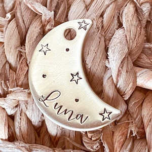 May include: Gold crescent moon-shaped pet tag with the name "Luna" engraved on it. The tag is decorated with small stars.