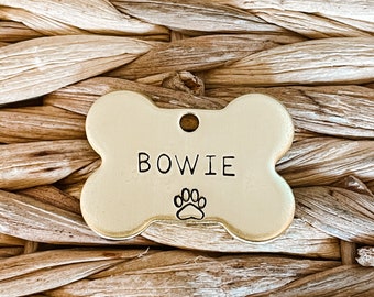 May include: Gold bone-shaped dog tag with the name "BOWIE" engraved on it and a paw print below the name.