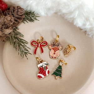 May include: Five gold Christmas themed stitch markers with red, green, and white enamel. The markers feature a reindeer, a stocking, a bow, a pine cone, and a Christmas tree.