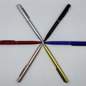 May include: Six ballpoint pens arranged in a starburst pattern. The pens are in various colors: silver, black, blue, red, gold, and rose gold. Each pen has a sleek, metallic finish and a clip.