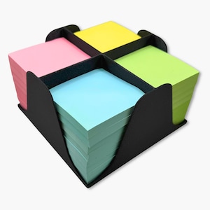 May include: A black desk organizer holding four stacks of square sticky notes in pink, yellow, green, and blue. The organizer has a square shape with curved sides and dividers to separate the note pads.