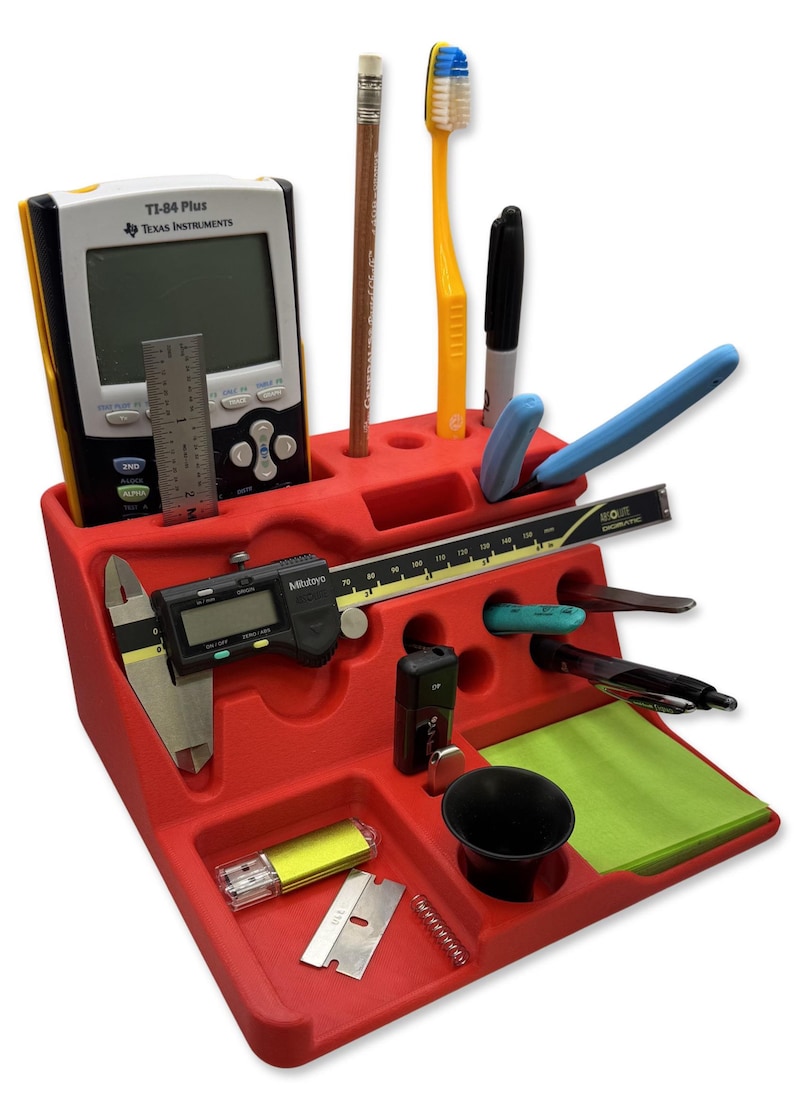 Puede incluir: Un organizador de escritorio rojo lleno de varios art&iacute;culos. Incluye una calculadora, l&aacute;piz, cepillo de dientes, bol&iacute;grafos, regla, calibrador digital, unidad USB y otras herramientas peque&ntilde;as. El organizador tiene m&uacute;ltiples compartimentos y ranuras.