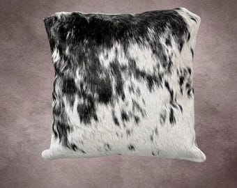 May include: Square decorative pillow with a cowhide pattern. The pillow features a natural black and white spotted design. The pillow is a square shape and appears to be made of a soft, textured material, perfect for home decor.