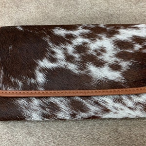 May include: A brown and white cowhide wallet with a brown leather trim.