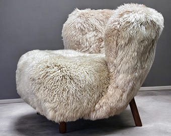 May include: A cream-colored, furry armchair with a curved back and seat. The chair has a plush, textured appearance and rests on four dark wooden legs. The design is modern and inviting, suitable for a living room or bedroom.