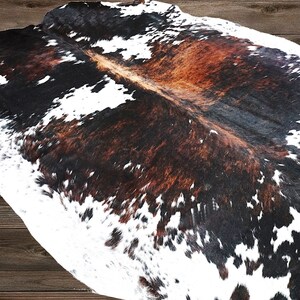 May include: A cowhide rug with a white, brown, and black pattern. The rug is made from natural cowhide and has a soft, luxurious feel.