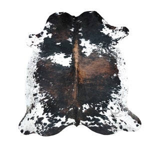 May include: A black and white cowhide rug with brown patches. The rug has a natural, rustic look and is perfect for adding a touch of Western style to any room.