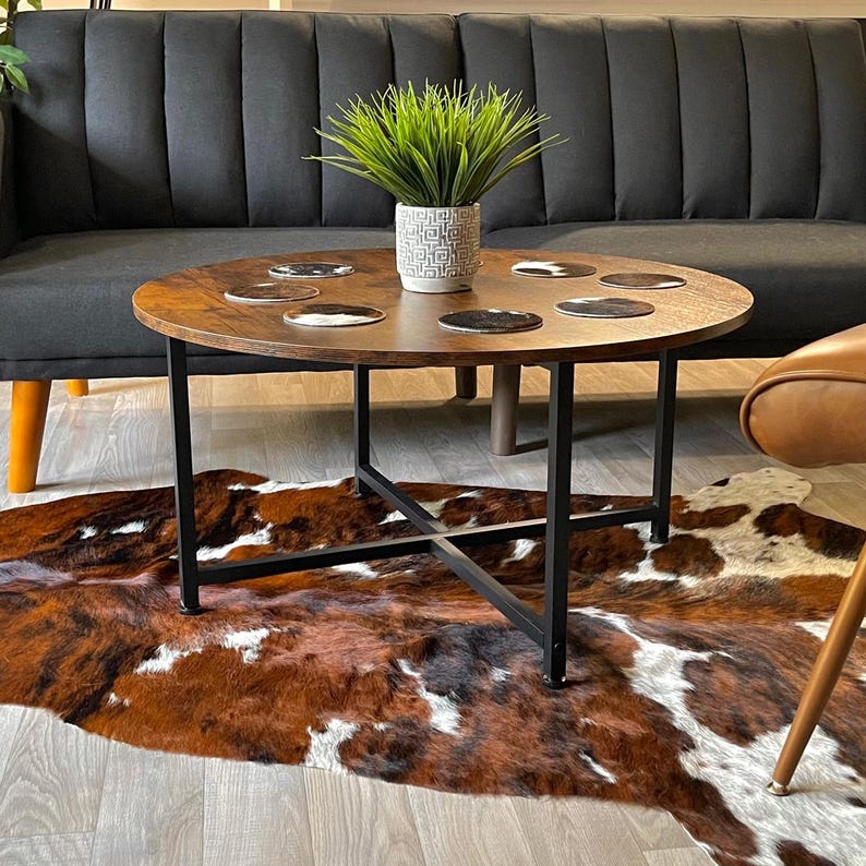 May include: A round wooden coffee table with a black metal frame and four legs. The table has a brown faux fur rug underneath and is decorated with a potted plant and several coasters.