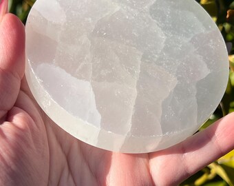 May include: A white selenite charging plate with a smooth, polished surface. The plate is round and has a natural, organic texture.