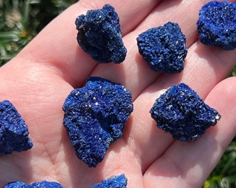 Puede incluir: Una colección de nueve pequeñas piedras de azurita azul rugosas. Las piedras son de varias formas y tamaños, y tienen una textura cristalina brillante.