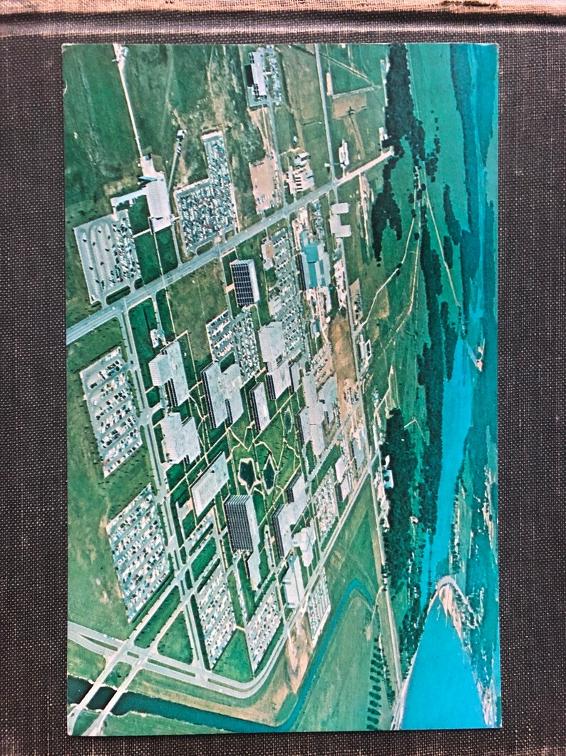 May include: An aerial view of a large industrial complex with multiple buildings, parking lots, and green spaces. The complex is surrounded by trees and a body of water.