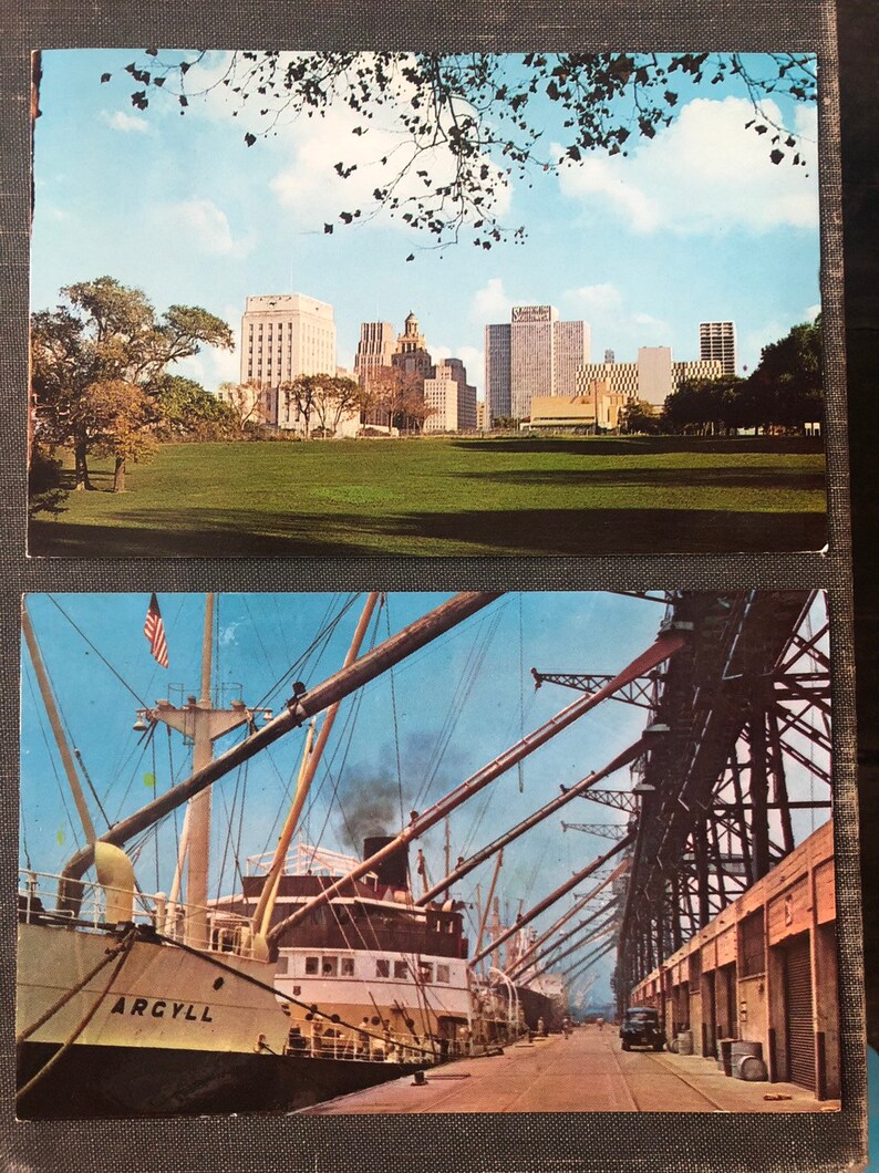 May include: Two vintage postcards. The top postcard shows a cityscape with tall buildings and a grassy park in the foreground. The bottom postcard shows a large cargo ship docked at a port with a metal structure overhead.