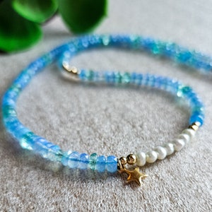 Peut inclure: Un collier d&eacute;licat en pierres pr&eacute;cieuses bleues et vertes avec une seule perle et un pendentif &eacute;toile en or.