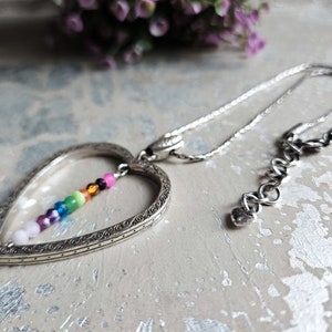 May include: A silver heart-shaped pendant necklace with a rainbow of small beads hanging inside the heart. The necklace has a silver chain and a lobster clasp.