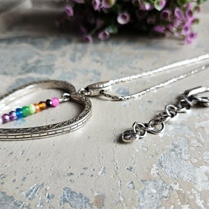 May include: A silver heart-shaped pendant necklace with a rainbow of small gemstone beads inside the heart. The chain is silver and has a lobster clasp.