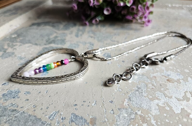 May include: A silver heart-shaped pendant necklace with a rainbow of small gemstone beads inside the heart. The chain is silver and has a lobster clasp.