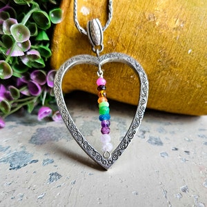 May include: A silver heart-shaped pendant necklace with a rainbow of gemstone beads hanging inside. The pendant has an ornate design around the edge.