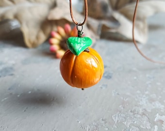 May include: A handmade orange ceramic pendant with a green leaf charm, hanging from a brown cord necklace.
