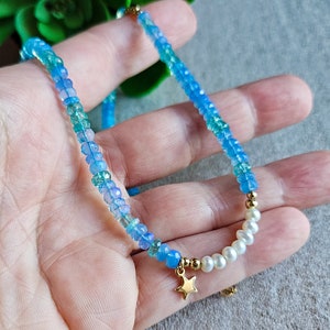 Peut inclure: Un collier d&eacute;licat en perles bleues et vertes avec un pendentif &eacute;toile en or et des accents de perles blanches.