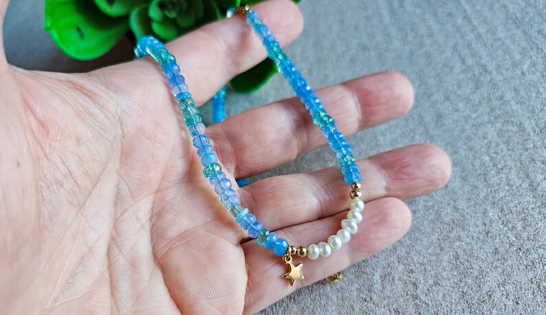 Peut inclure: Un collier d&eacute;licat en perles bleues et vertes avec un pendentif &eacute;toile en or et des accents de perles blanches.