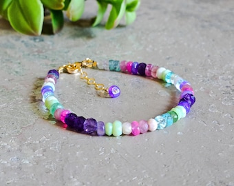 May include: A colorful beaded bracelet with a gold clasp. The bracelet features a variety of gemstones in shades of purple, pink, green, and blue.