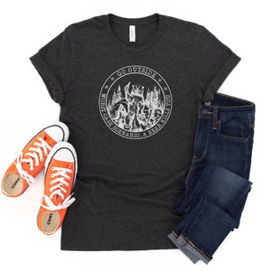 Könnte beinhalten: Ein dunkelgraues T-Shirt mit einem weißen Grafikdesign eines Bären in einem Wald. Das Grafikdesign enthält den Text "Go Outside Worst Case Scenario, A Bear Kills You".