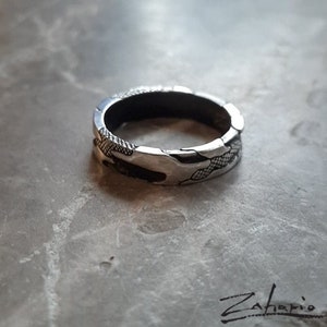 以下が含まれることがあります： テクスチャ加工が施された模様のある銀の指輪。指輪は幅広で丸みを帯びています。