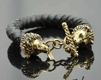 May include: A black leather braided bracelet with two gold lion head clasps. The bracelet has a toggle clasp.