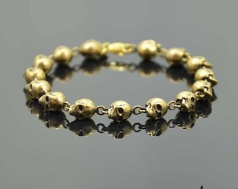May include: A gold bracelet made of a chain of linked skull charms.