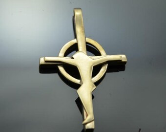 May include: A gold-toned pendant featuring a stylized depiction of Jesus Christ on a cross with a circular halo. The pendant is made of metal and has a smooth, polished finish.