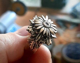 May include: A silver ring with a detailed design of a sunflower with a small diamond in the center.
