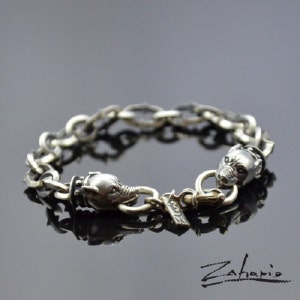 May include: A silver bracelet with two wolf head charms and a silver clasp. The bracelet is made of a thick chain link design.