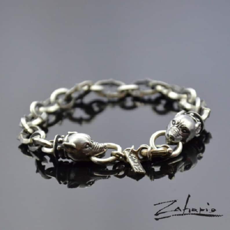 May include: A silver bracelet with two wolf head charms and a silver clasp. The bracelet is made of a thick chain link design.