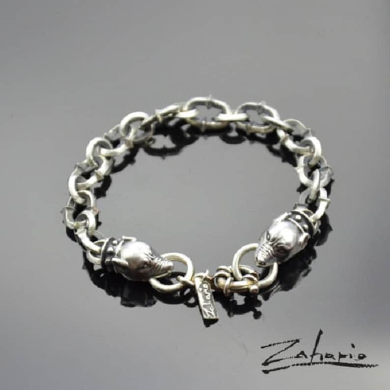 May include: Silver bracelet with a chain link design and two animal head charms. The chain has small spikes along the links. The bracelet has a silver clasp with the word "Zahapio" engraved on it.